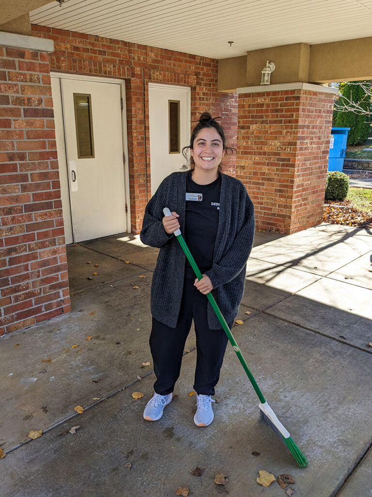 Staff members sweep away leaves on the sidewalk in the senior living community.