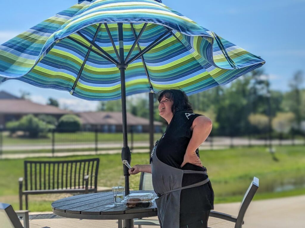 Employee adjusting a large striped umbrella on a sunny patio to provide shade and stay cool.