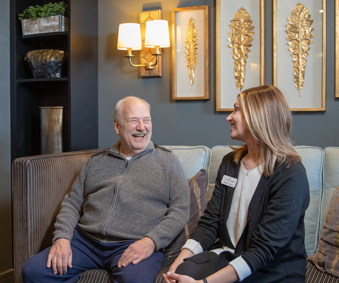 A woman and an older man are sitting in the Library at The Town and Country Senior Living.